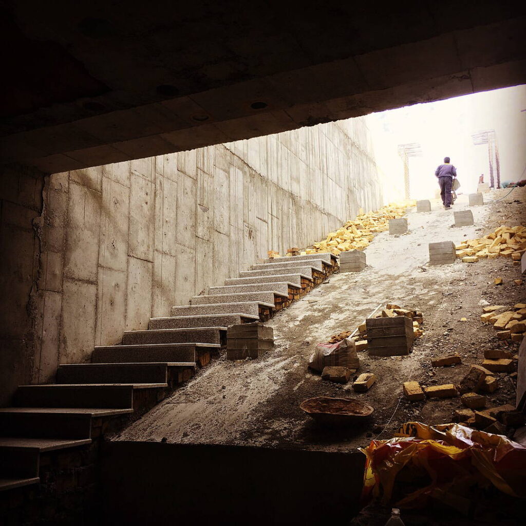 Completed concrete stair and ramp structure in a deep trench, with a worker walking toward the bright opening at the top.