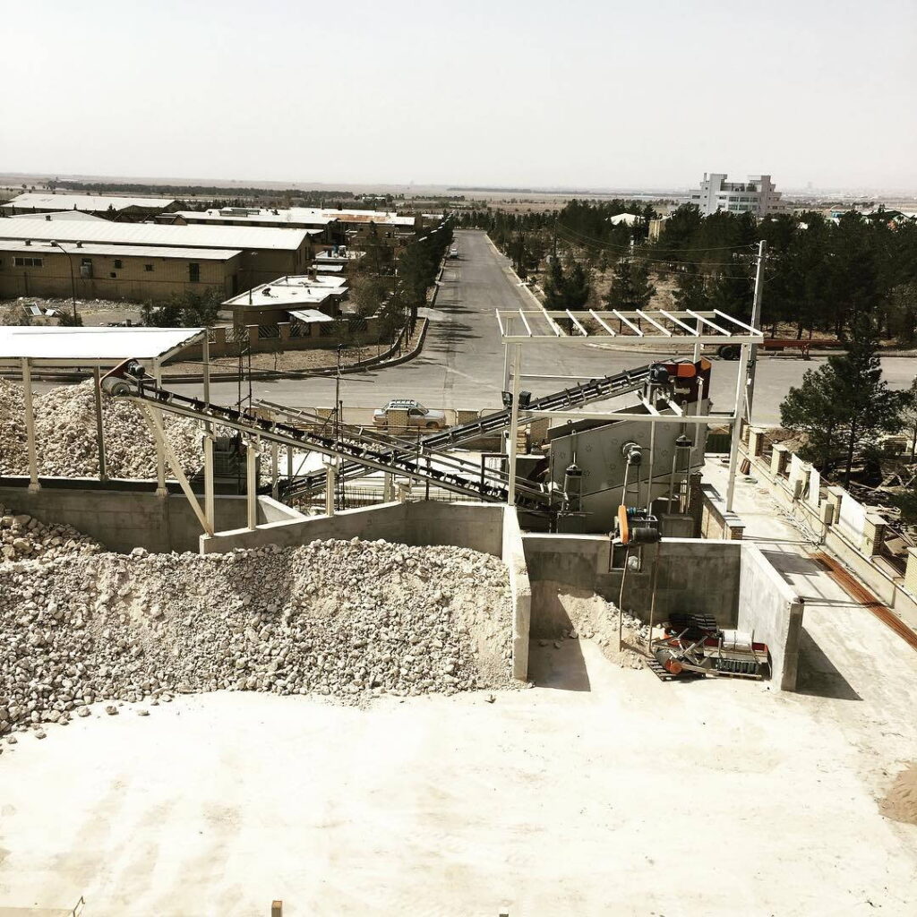 Overview of an aggregate crushing and conveying installation with conveyors feeding into bunkers beside an access road.