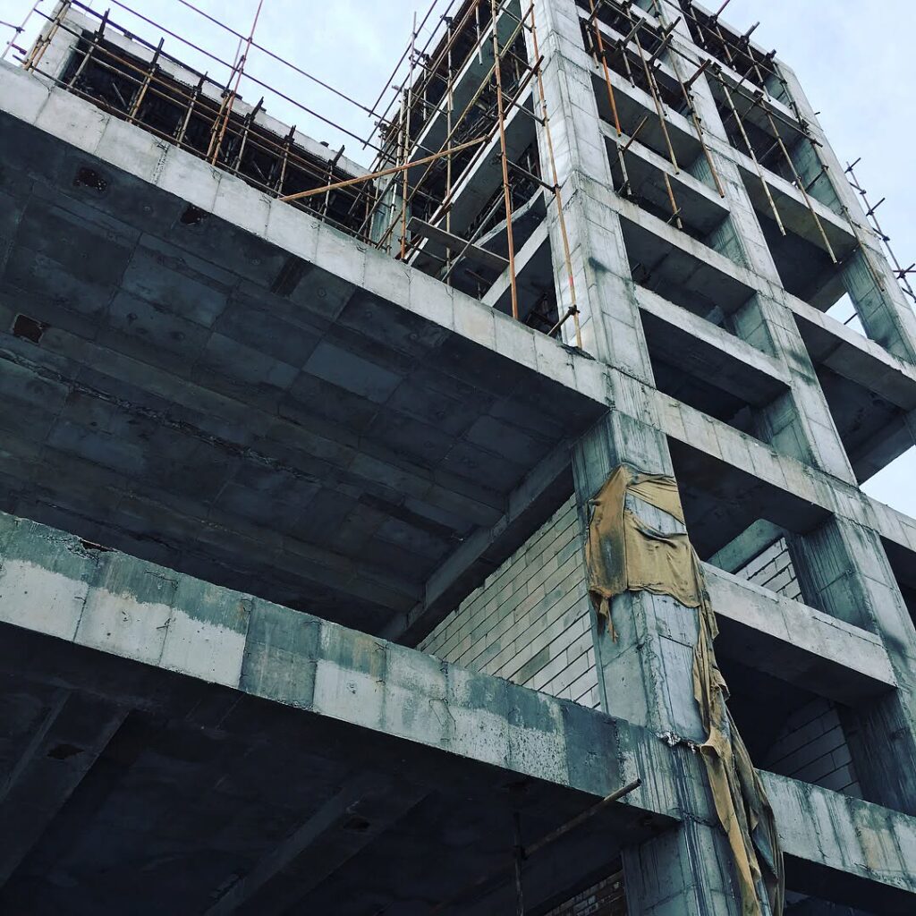 Upward view of a tall reinforced concrete frame with scaffolding along the upper levels for the Industrial Complex Design facility.