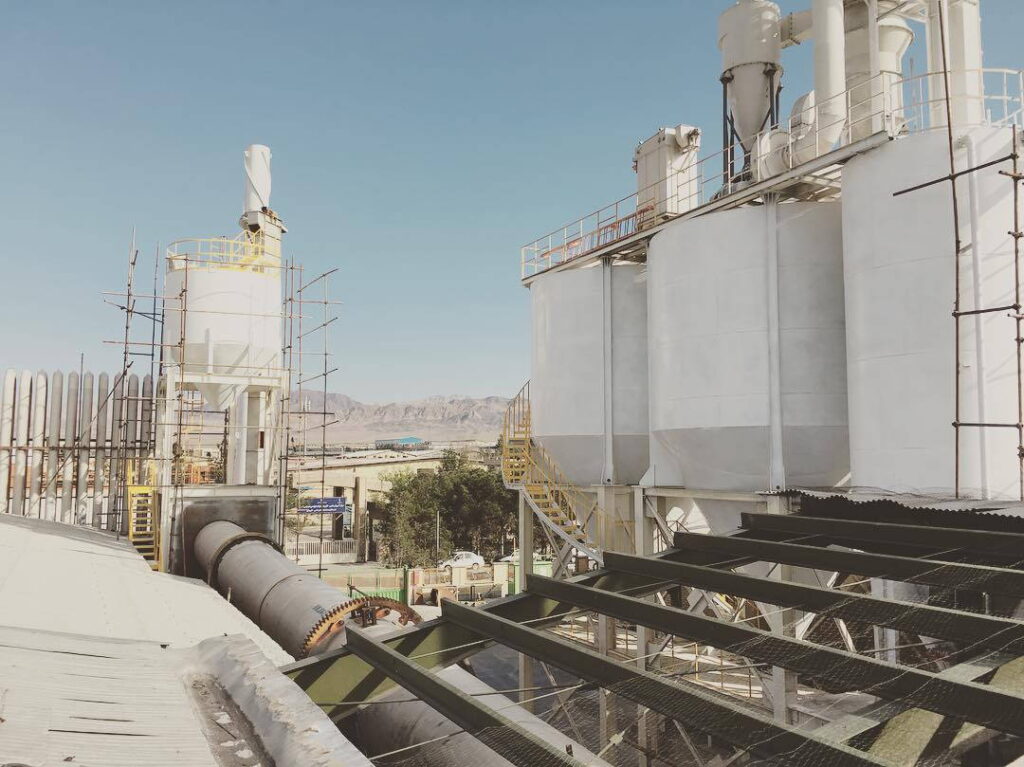 Cluster of tall white process vessels and silos with access platforms and ducting in an industrial plant against a clear sky.