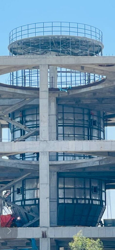 Poly aluminum chloride process tower under construction, showing a tall cylindrical vessel enclosed within a multi-story reinforced concrete frame with circular openings and top platform against a clear blue sky.
