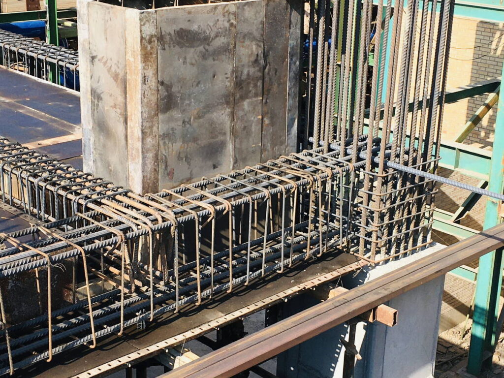 Close-up of dense reinforcing steel bars forming an L-shaped beam and column cage around a square column formwork at a building site.