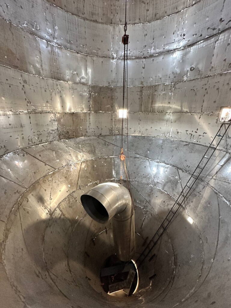 Wide-angle view looking down into a massive conical-bottom stainless steel chemical reactor.