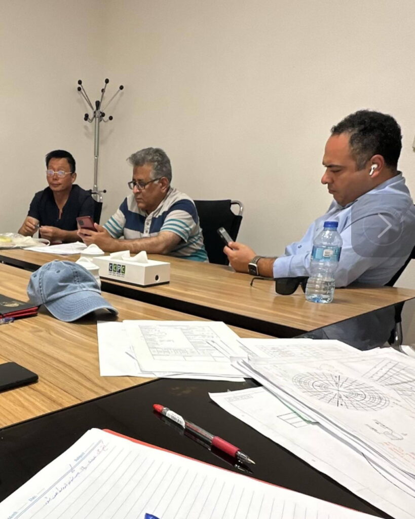 Three engineers reviewing technical blueprints and PAC project documents at a conference table.