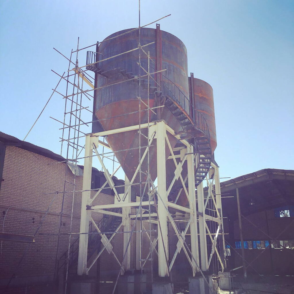 Two large industrial steel silos mounted on a white reinforced structural frame with scaffolding.
