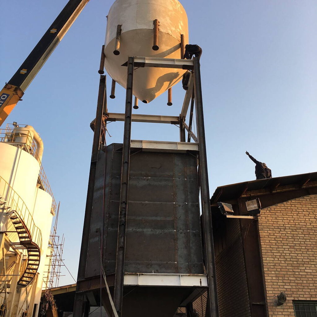 Crane-assisted installation of a conical steel tank onto a multi-tier structural frame.