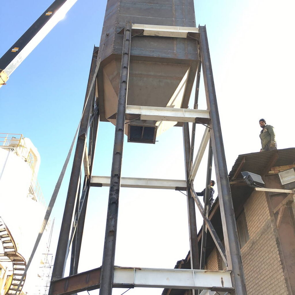 High-angle view of a vertical steel support tower holding a conical chemical vessel.