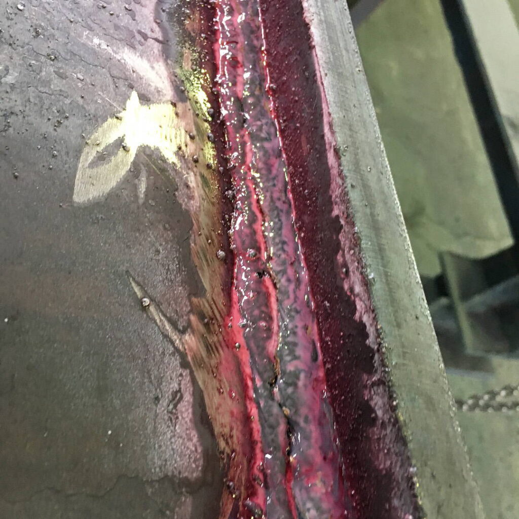 Close-up of a welded joint covered in pink dye for liquid penetrant inspection (LPI).