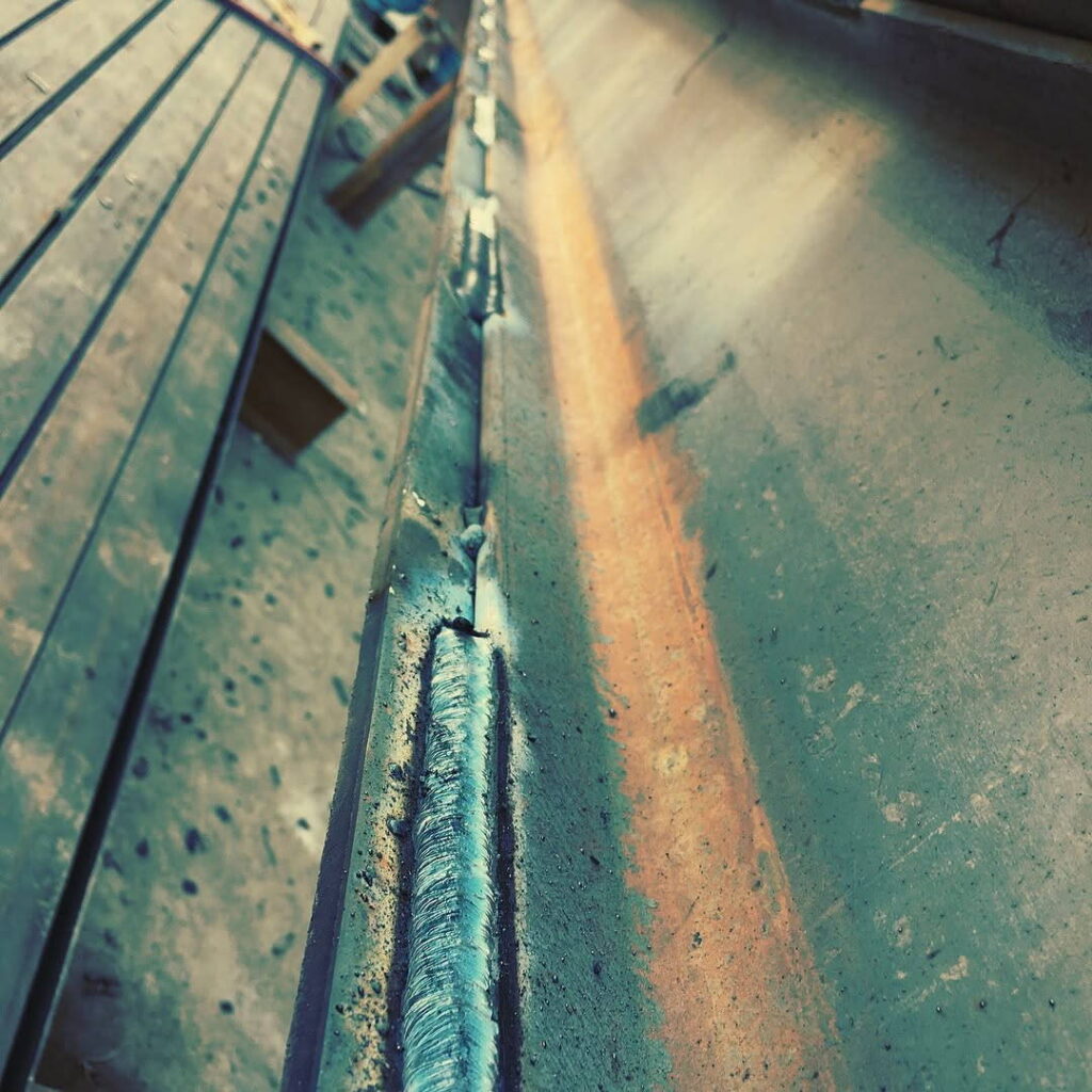 Vertical perspective of a long, clean industrial weld bead joining two thick steel plates.