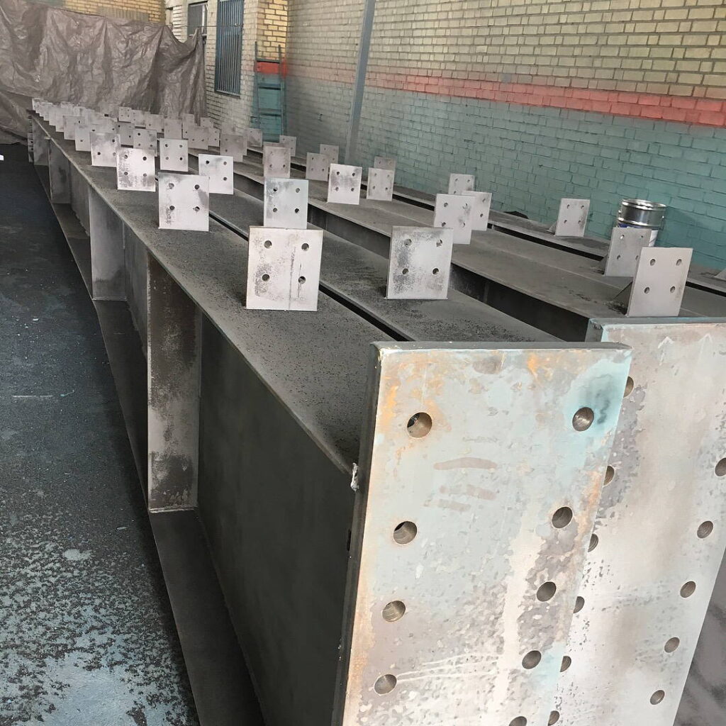A row of identical steel beams with pre-drilled connection plates ready for assembly.