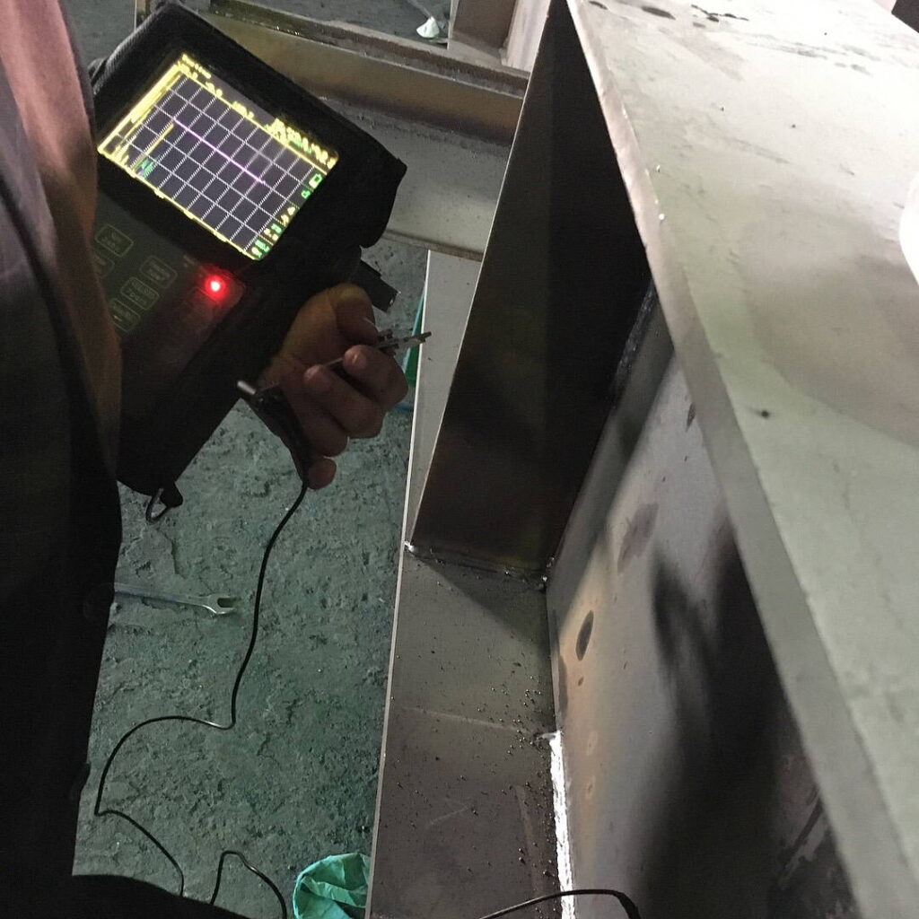 A technician holding an ultrasonic testing (UT) device against a steel weld seam.