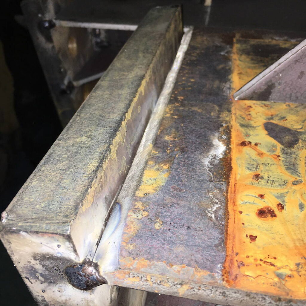 Close-up of a heavy fillet weld at a 90-degree intersection of two thick steel plates.