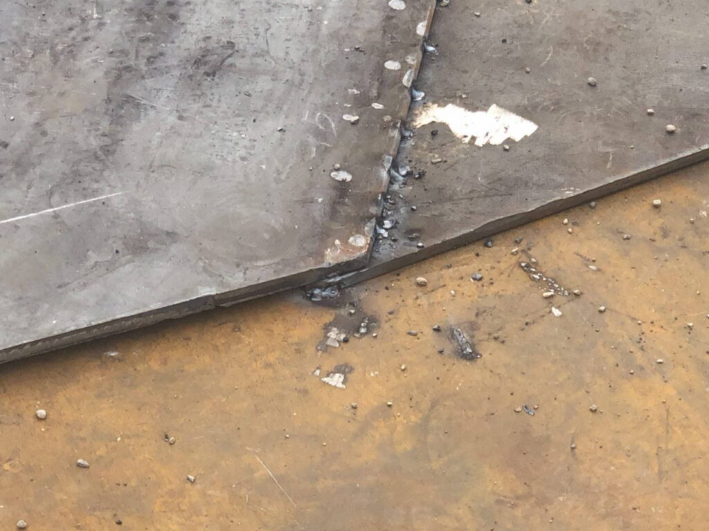Close-up of two thick steel plates being aligned for a tack weld on the floor of a tank.