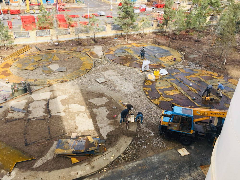 Aerial view of a construction site with three large circular tank foundations and a blue crane.