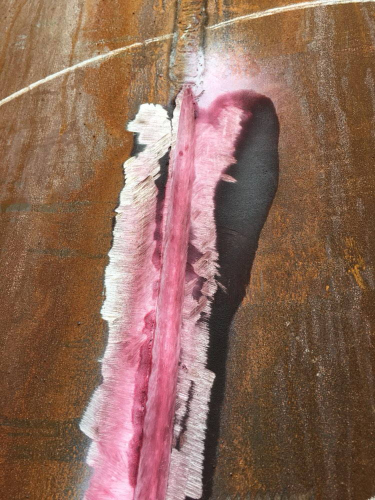 Close-up of a pink dye penetrant test on a vertical tank shell weld.