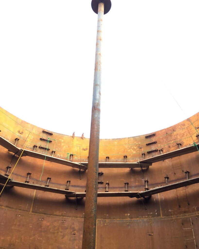 Looking up from inside a steel tank at a central support pillar and circular scaffolding.