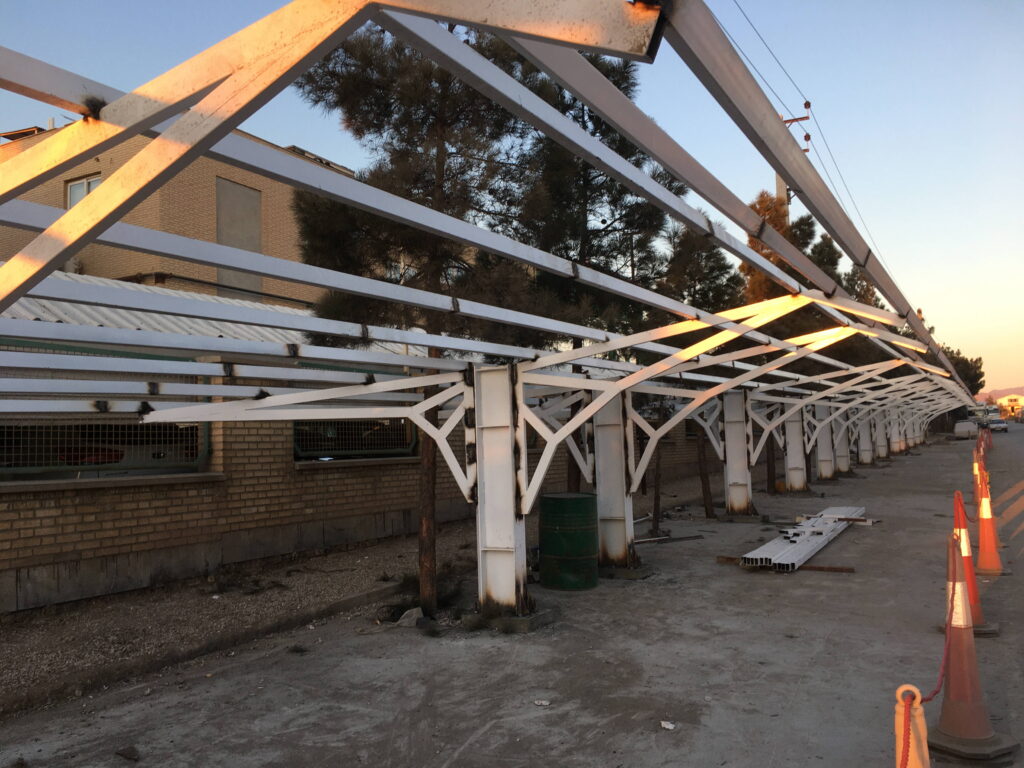 Long white steel canopy frame supported by a line of columns along an industrial site access road at sunset.