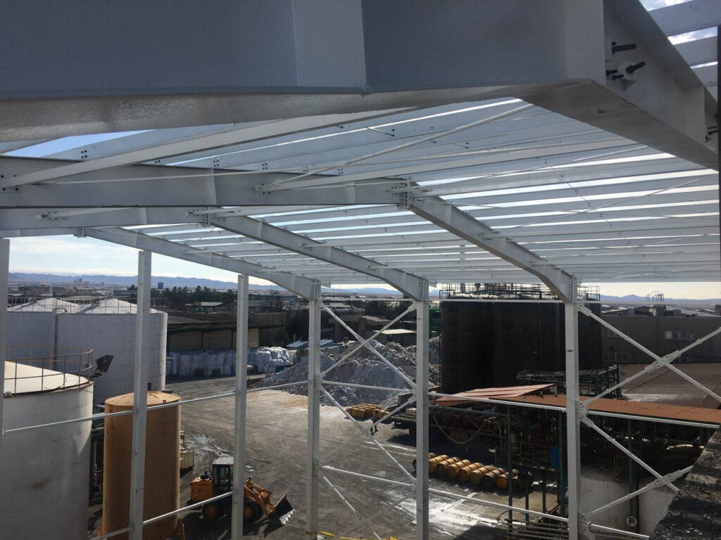 White painted steel portal frame structure under construction overlooking storage tanks and industrial yard.